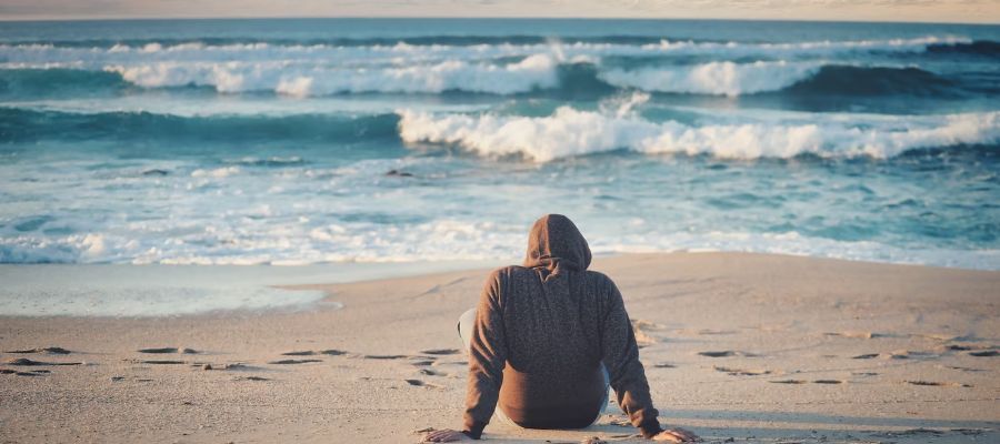 yalnız ve mutsuz şekilde sahilde oturan sırtı dönük bir kişi
