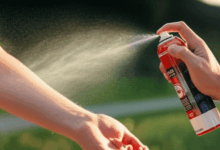 a hand applying insect repellent spray on an arm in an outdoor setting at dusk create in horizontal format do not write text on image