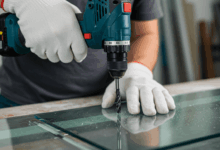 close up of a hand wearing protective gloves and glasses using a drill on glass create in horizontal format do not write text on image