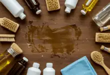 top down shot of various cleaning products like oils solvents and brushes arranged neatly around a stubborn wax stain on a wooden table with a microfiber cloth ready for use natural and bright studio lighting